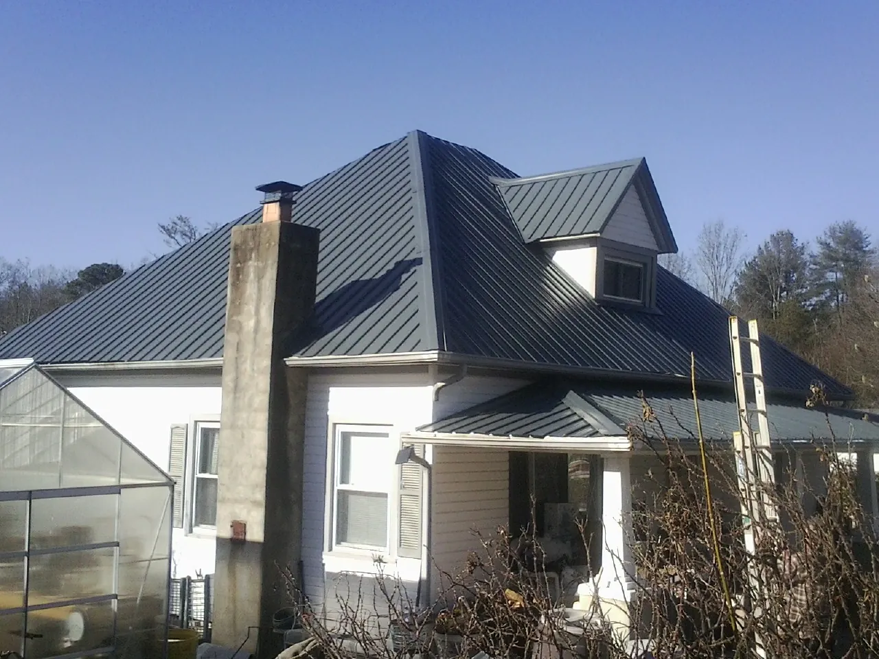 Dark blue standing seam metal roof on a white farmhouse with dormer — Slate & Tile Roof Repair by Roofing Brothers in Mountain Ranch