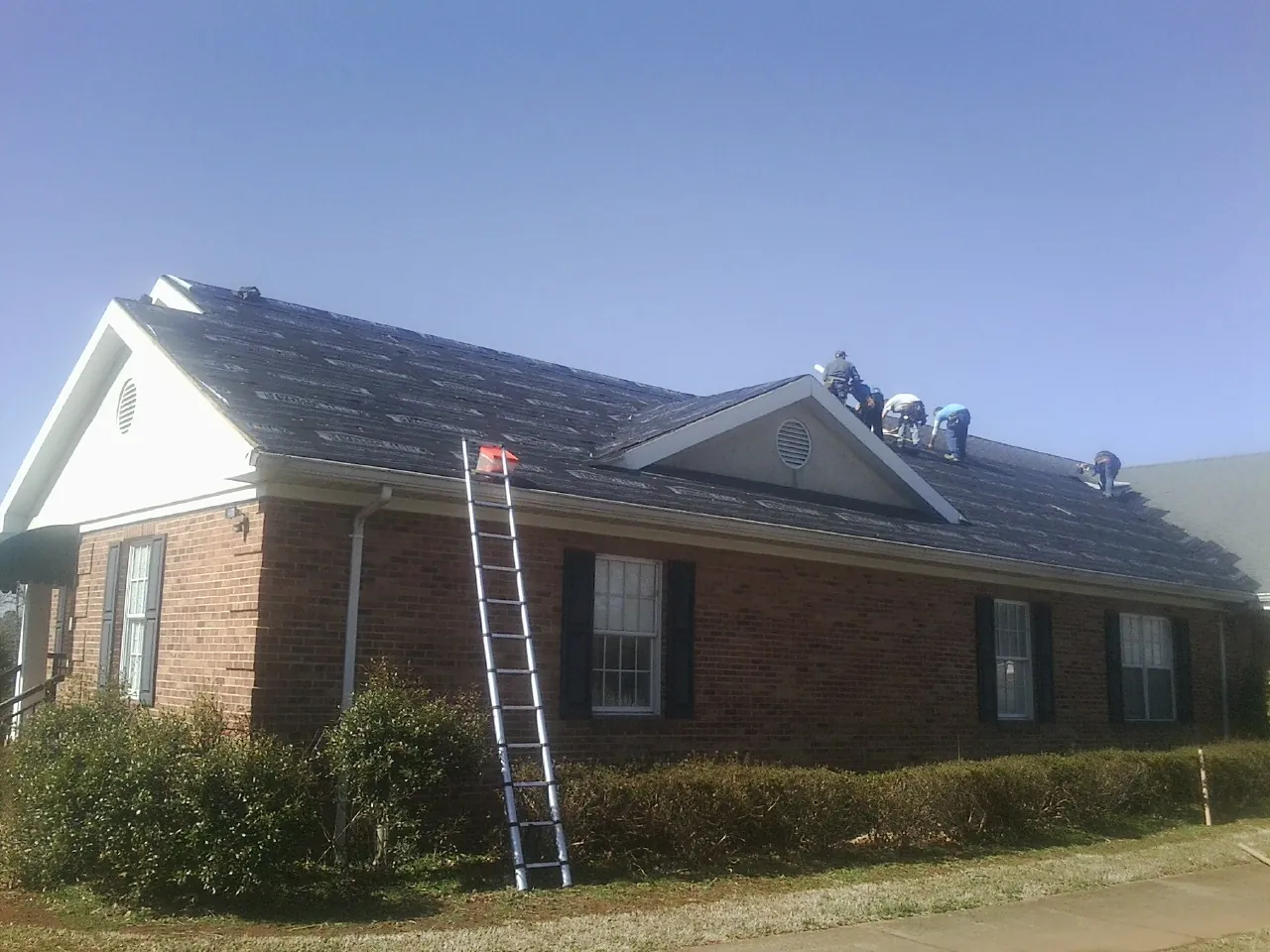 Crew tearing shingles off a brick ranch roof with a ladder set — Metal Roof Repair work by our crew in Mountain Ranch