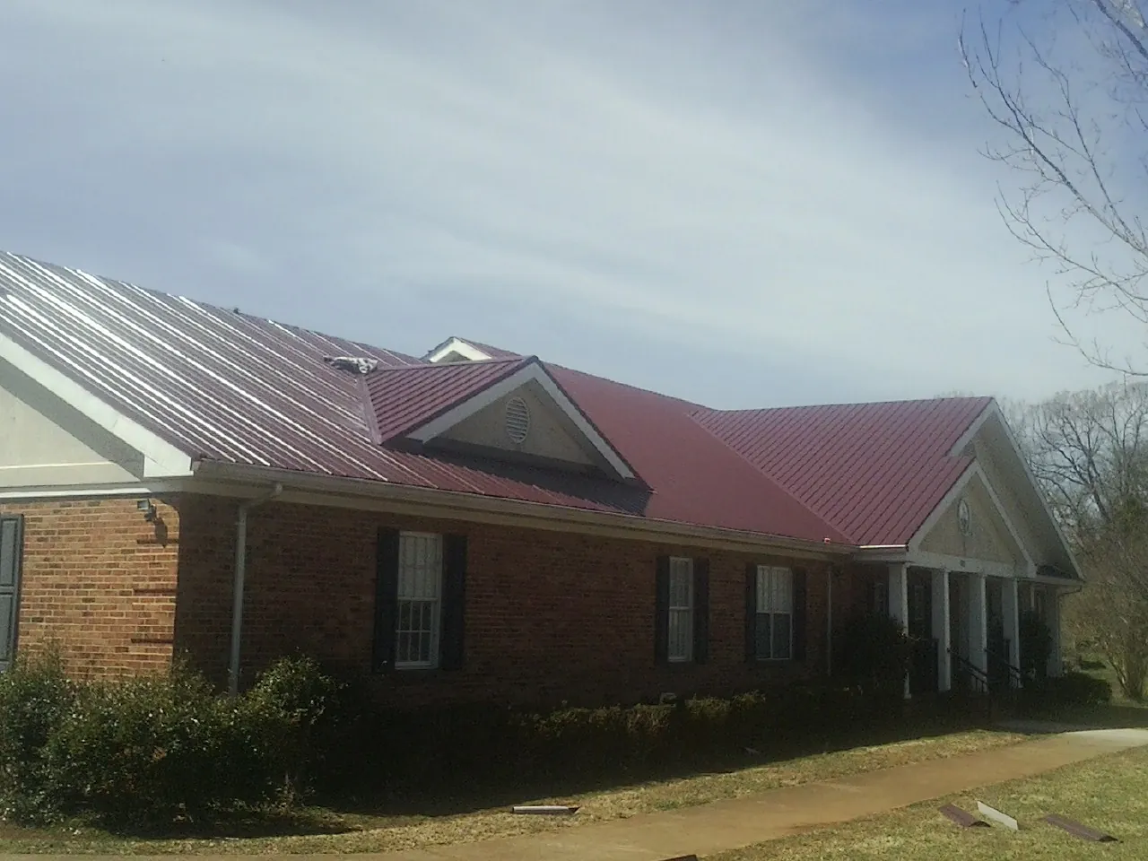 Red metal roof with gabled entries on a long brick building, from a Hail Damage Roof Repair job in Mountain Ranch