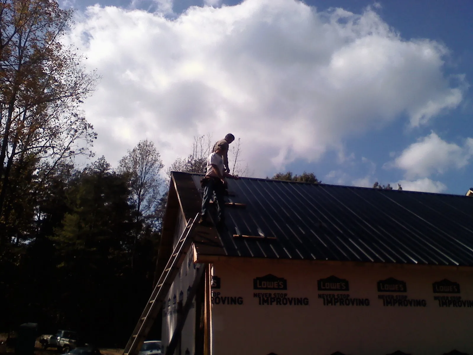 Roofer fastening dark metal panels high against a cloudy sky, from a Roof Inspection job in Mountain Ranch