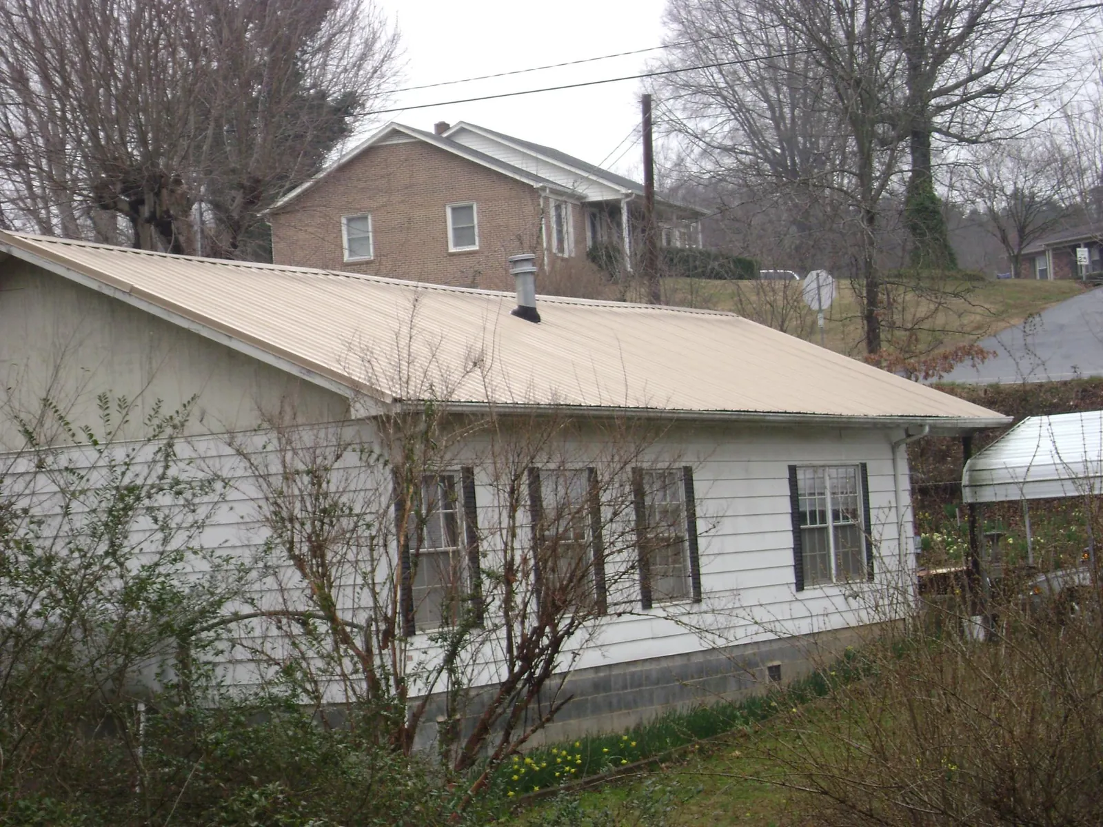 Tan metal roof on a white sided house set into a hillside — Commercial Roofing by Roofing Brothers in Mountain Ranch